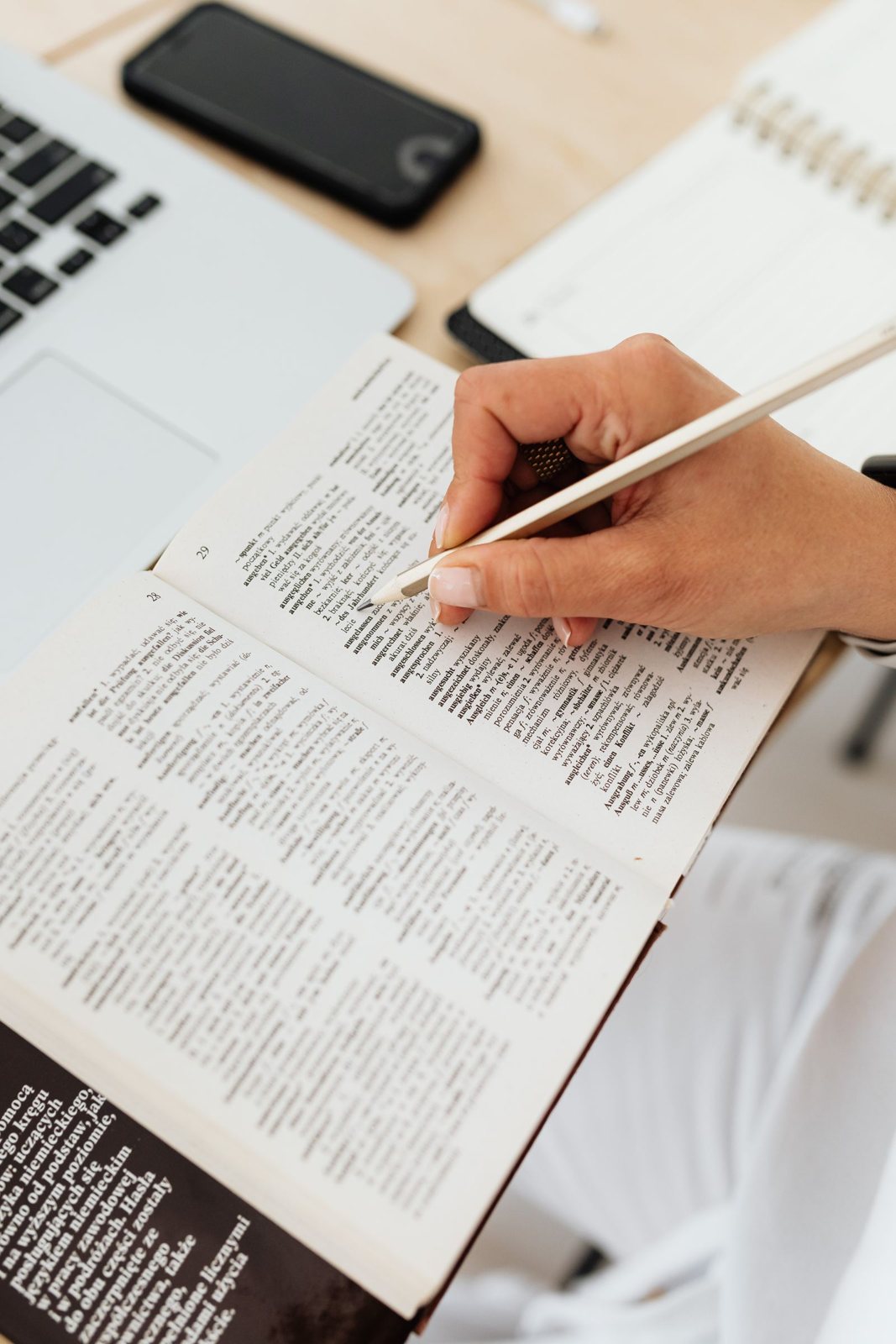 A translator marking up a dictionary beside a laptop and notes